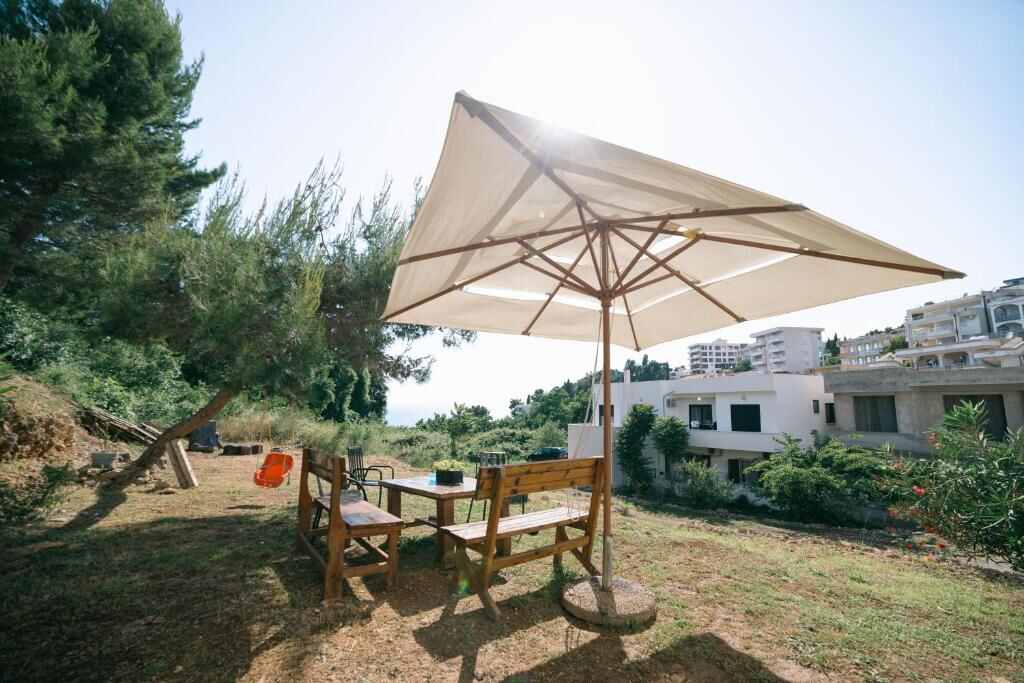 Garden with a large parasol, wooden table and benches at Lungo Mare Ulcinj